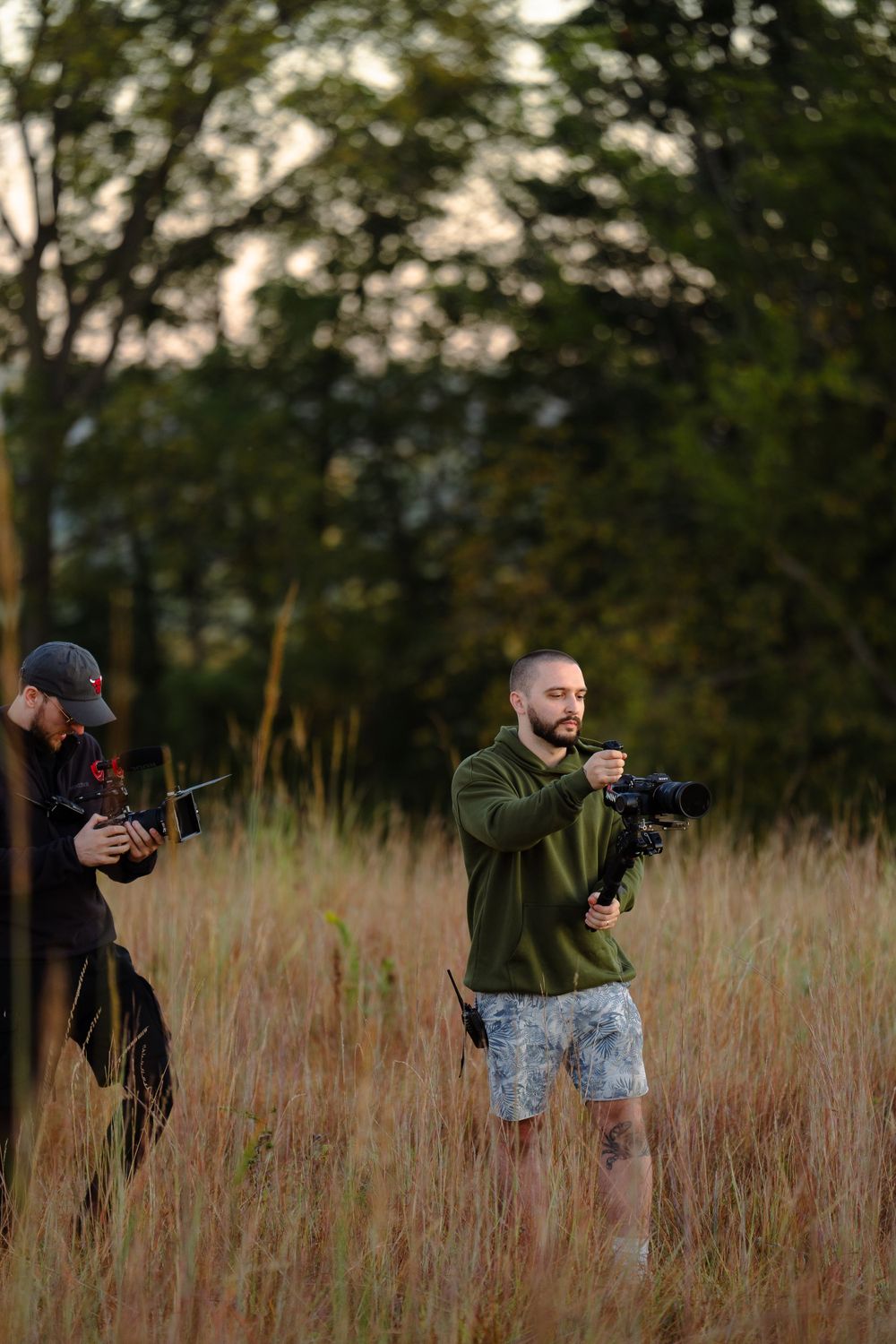 Two photographers shooting with professional cameras in tall grass during golden hour.