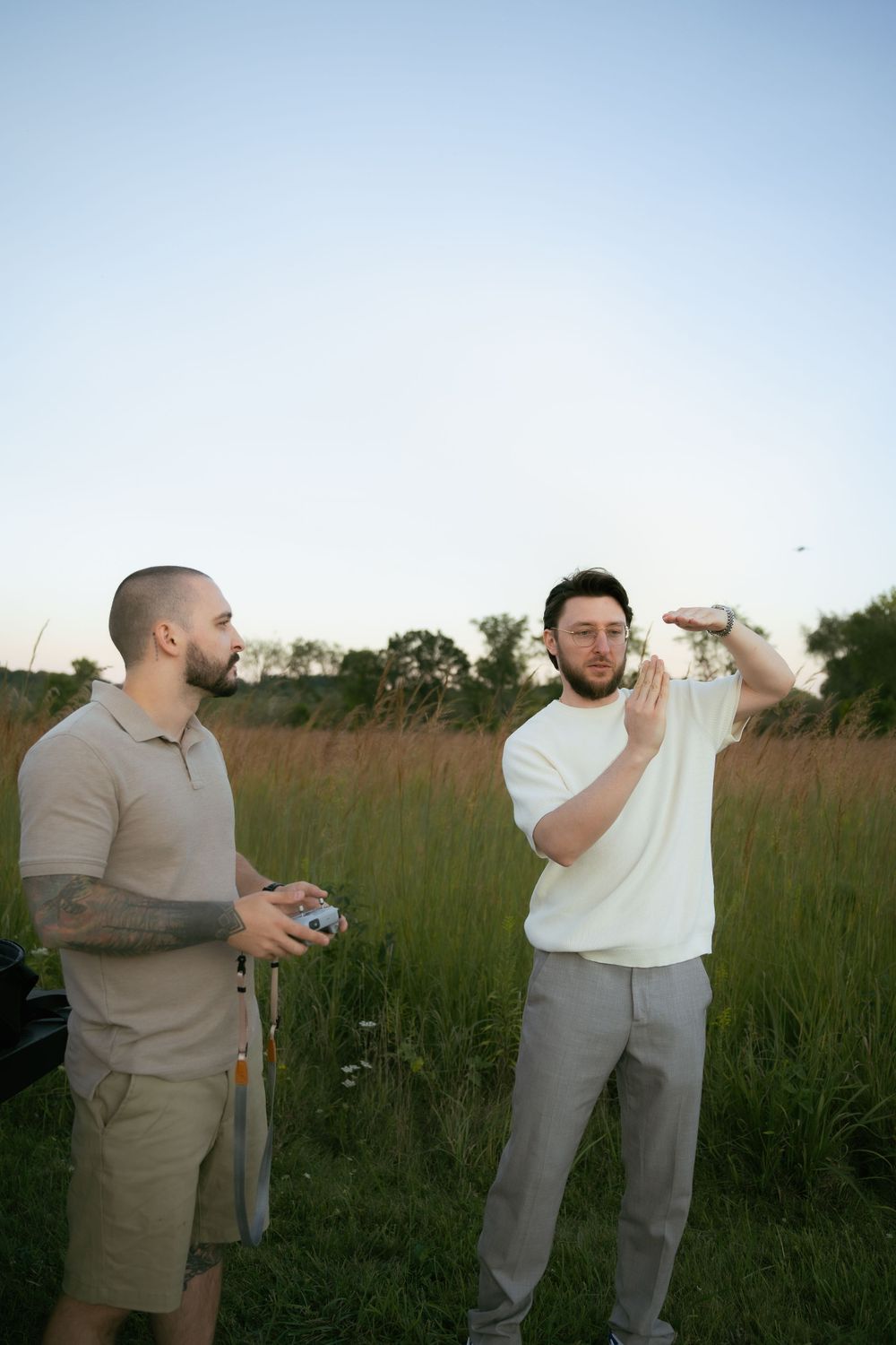 Two people operating camera equipment in a field during golden hour.