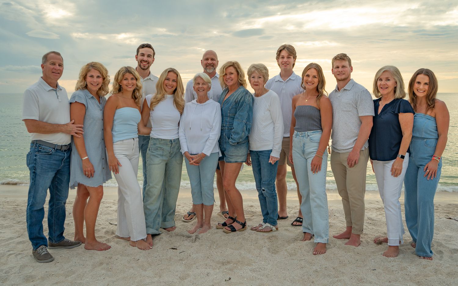 Extended family group portrait at sunset on a white sand beach wearing coordinated blue and white outfits.