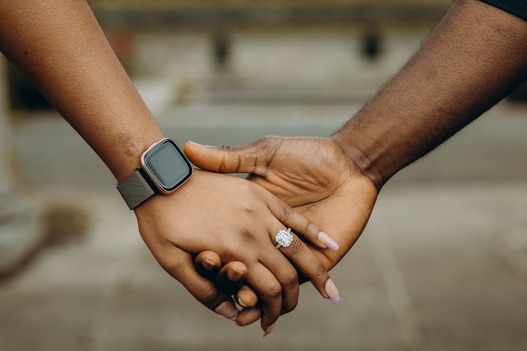 Close-up of two hands clasped together, one wearing a smart watch and engagement ring.
