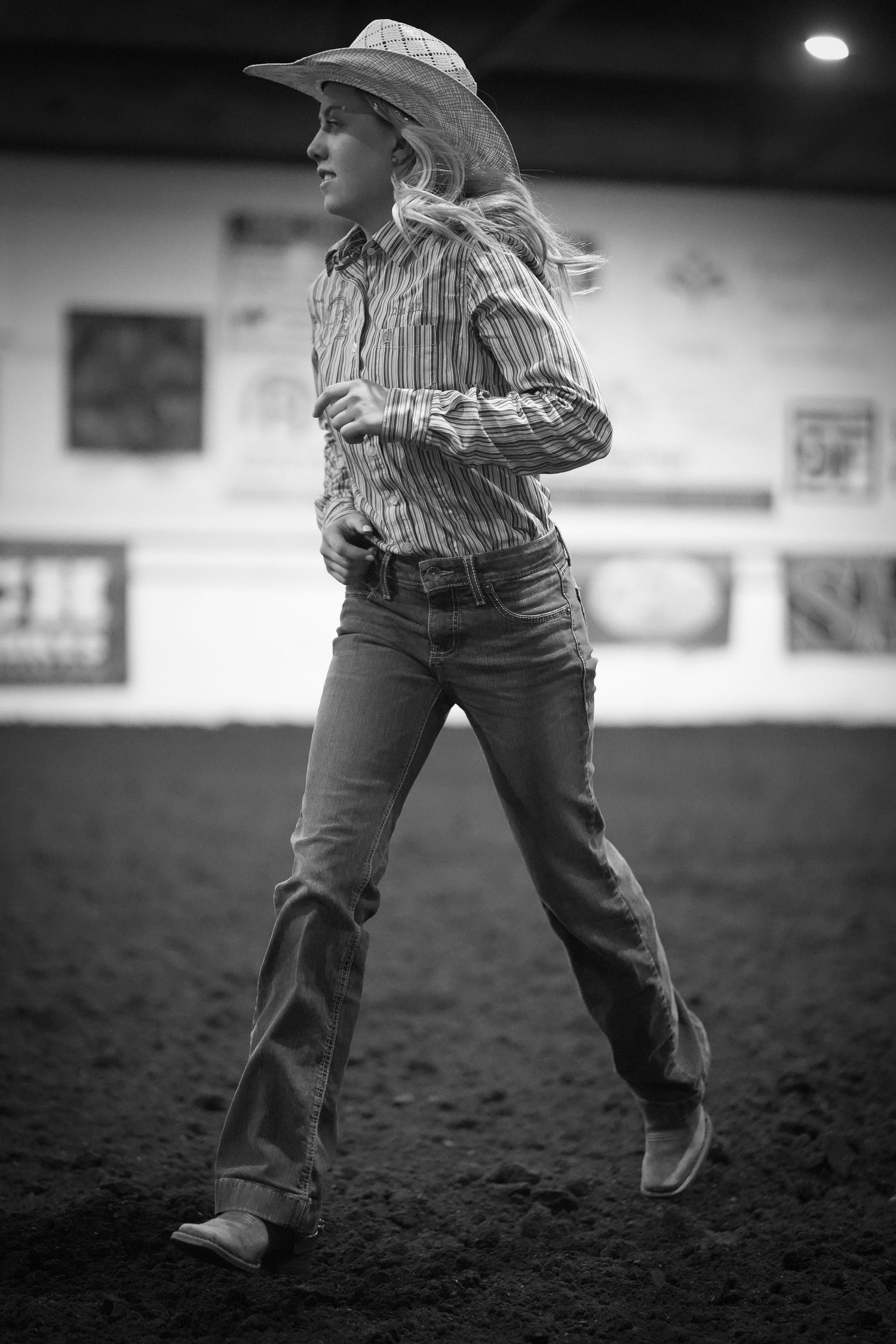 Black and white photo of a person in western attire running across a dirt arena during a rodeo event.