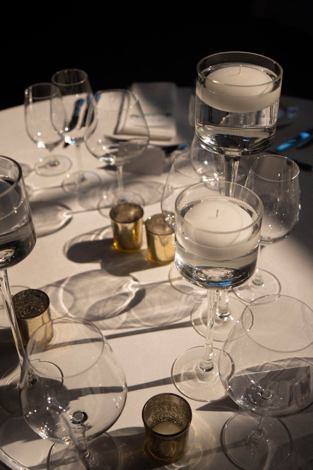 Elegant table setting with wine glasses and candles casting dramatic shadows on white tablecloth.
