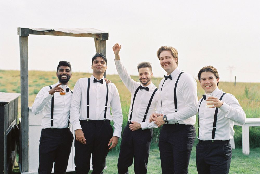 Groomsmen in suspenders and bowties posing under wooden arch.