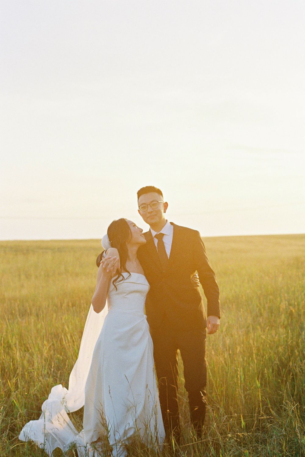A romantic sunset photo of newlyweds embracing in a golden wheat field during their wedding photoshoot.