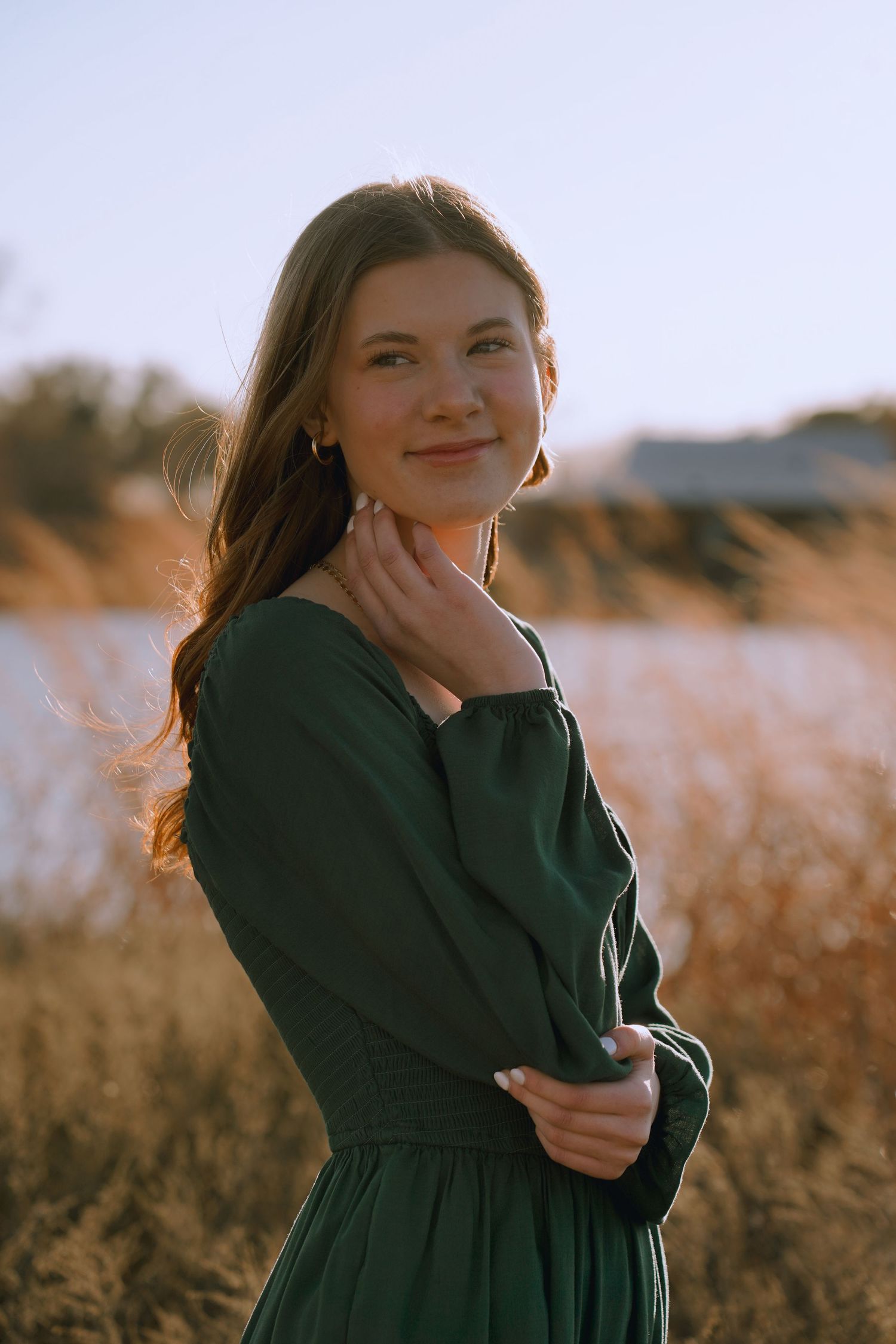 Portrait in emerald green dress standing in a sunlit field of golden grass during sunset.