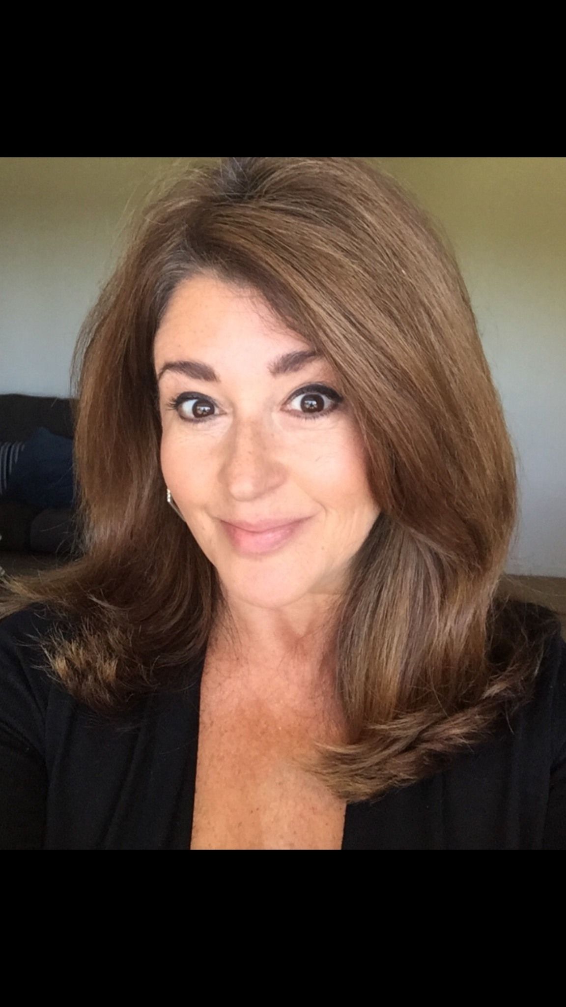 Professional selfie with a warm smile showcasing voluminous brown hair and a black top.