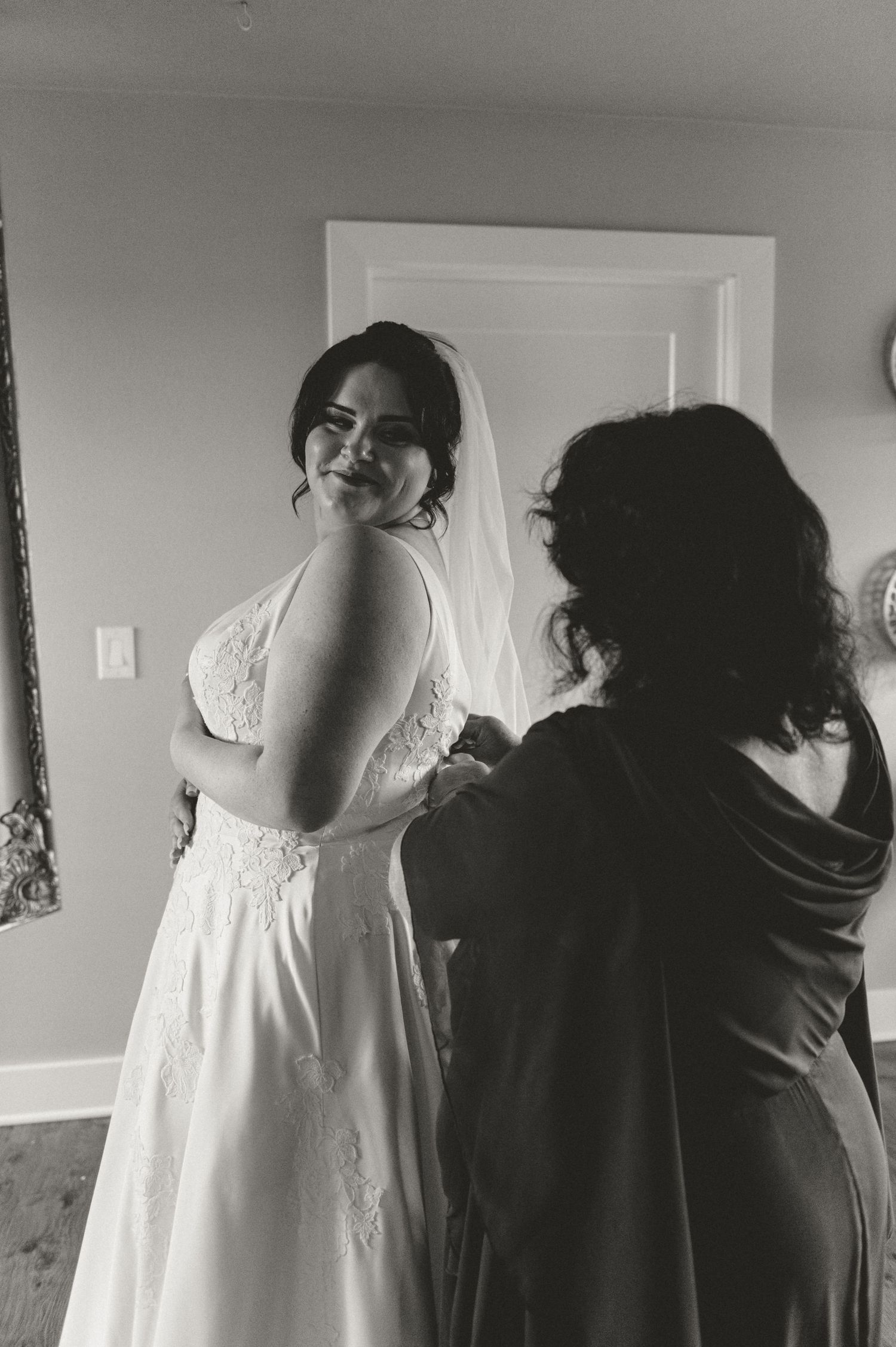 A bride in a white lace wedding dress smiles during final preparations.