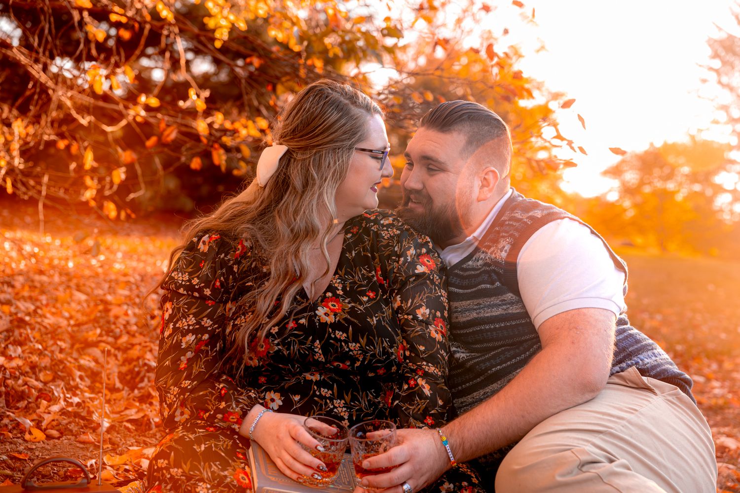 Romantic couple sitting together during golden autumn sunset with glowing foliage in background.
