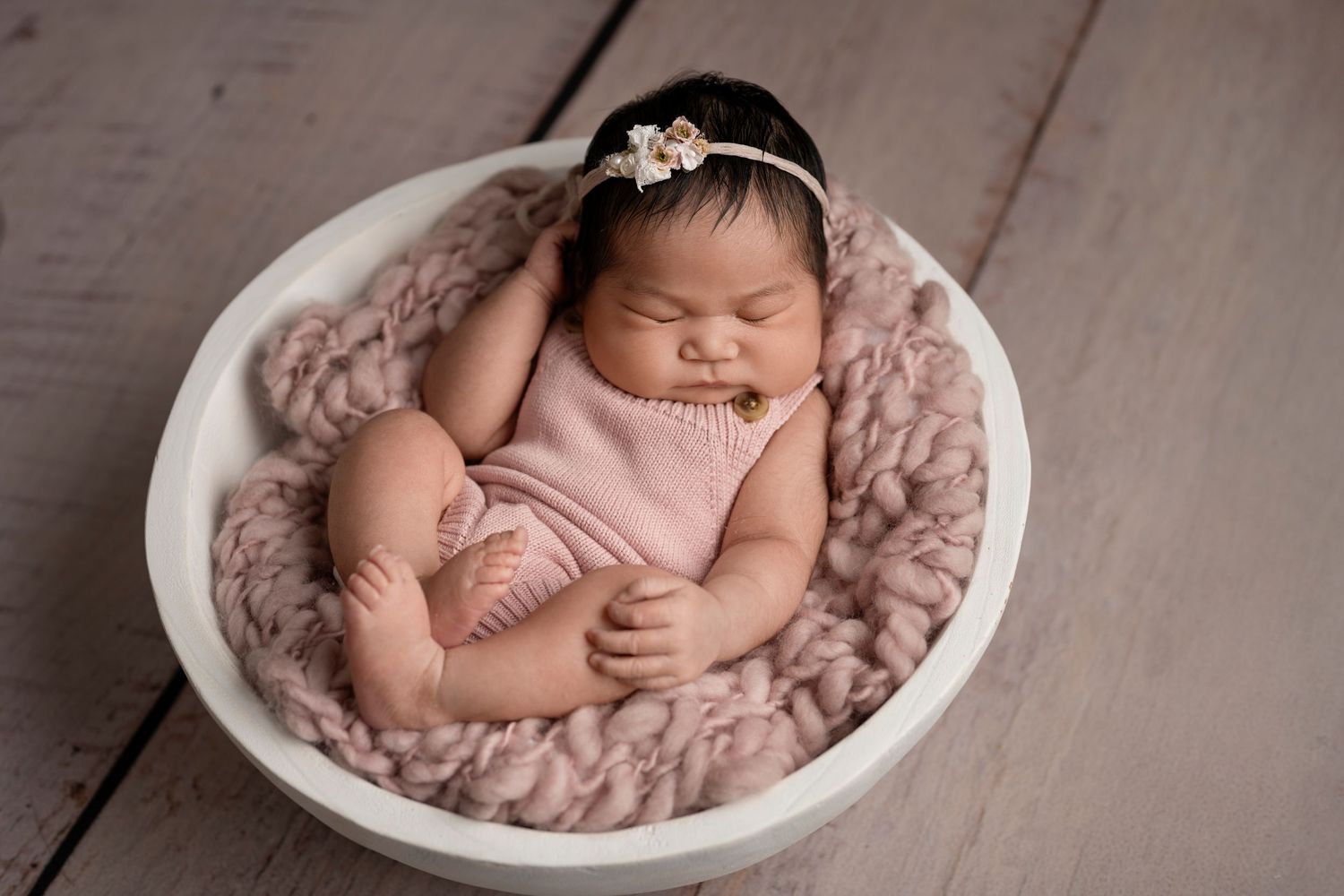 Sleeping newborn posed in white bowl with pink blanket for her studio photography session.