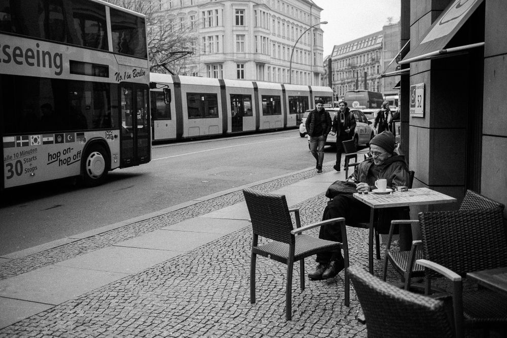 City tram and sightseeing bus pass outdoor cafe seating on cobblestone street.