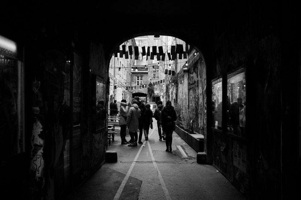 Dark archway passage with silhouettes of people walking through a historic tunnel.