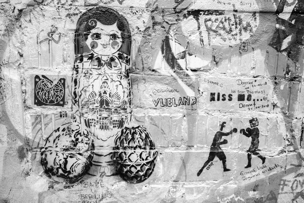 Street art mural on a wall with graffiti tags visible in the background.