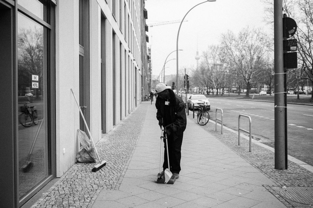 Street scene of a person sweeping a sidewalk along a modern building facade.