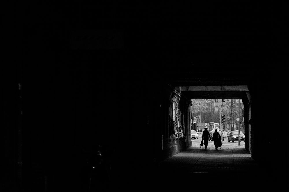 Black and white image of people walking through a dark tunnel into bright daylight.