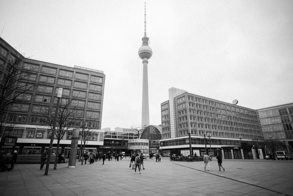 Berlin's Alexanderplatz with TV Tower rising above modernist buildings in black and white.
