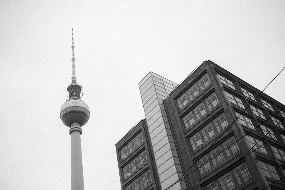 Berlin TV Tower rises dramatically against modern building facade in monochrome.
