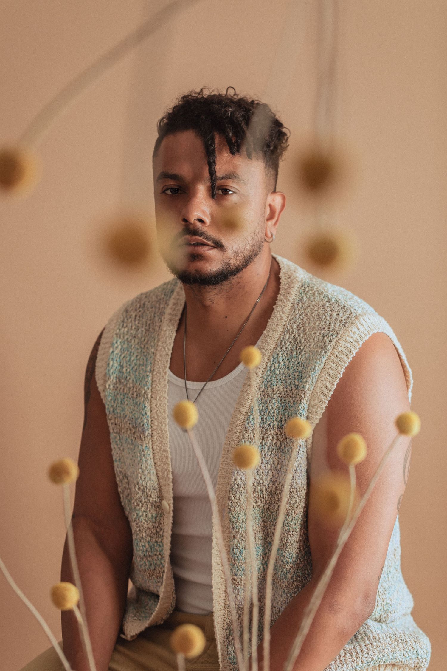Artistic portrait featuring knit vest and floating yellow elements against neutral background.