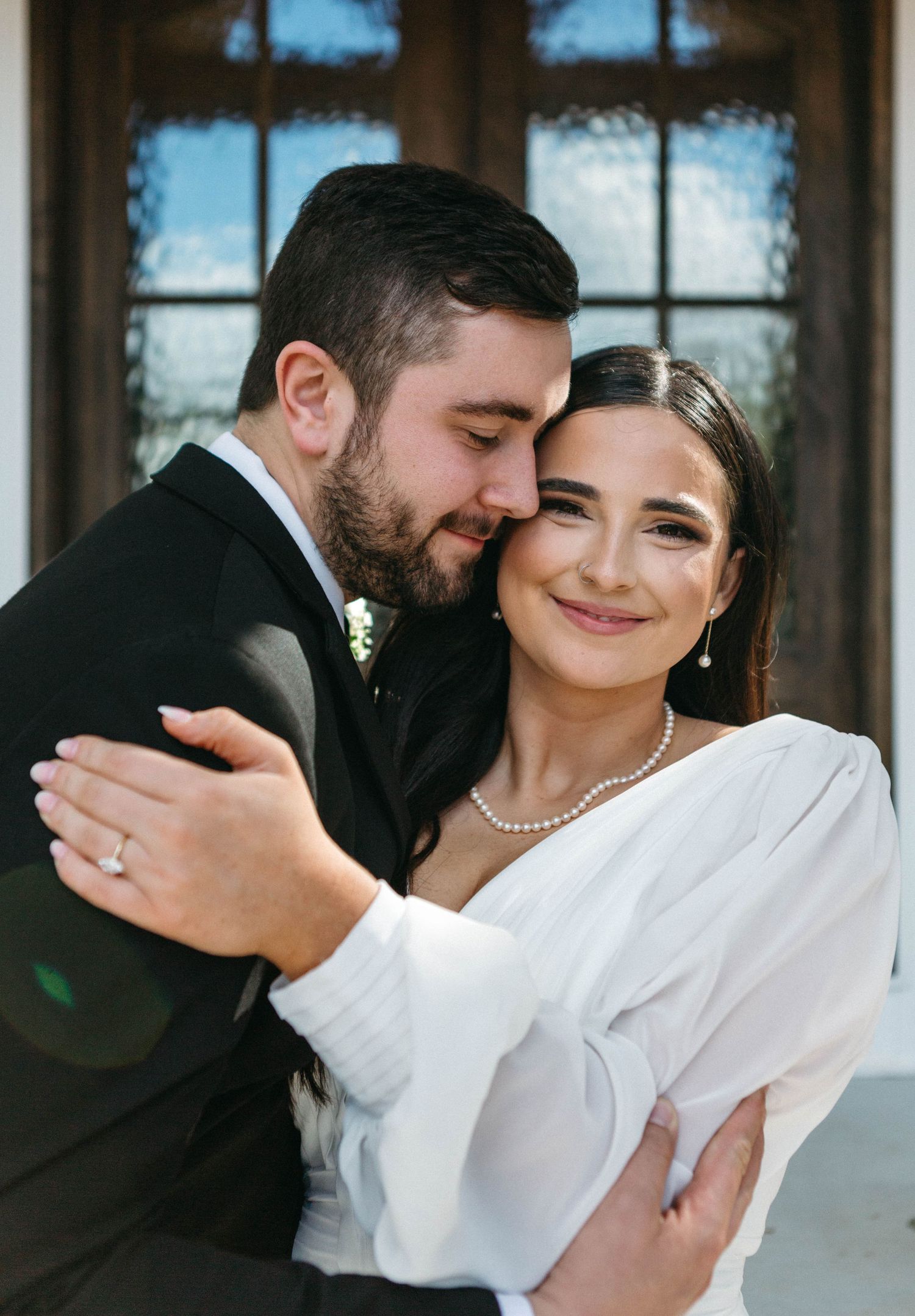 A tender embrace between newlyweds, with the bride in white and groom in black against an elegant backdrop.