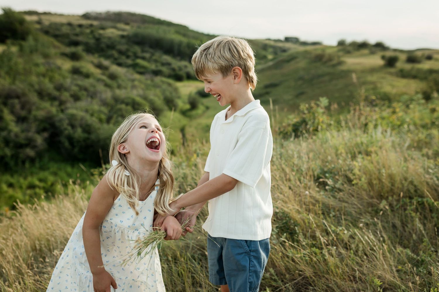 Siblings laughing together in the rolling hills at golden hour during a family photography session in Calgary