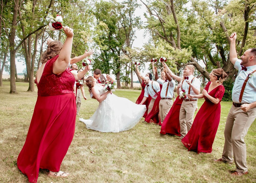 Wedding party in red and white attire poses playfully on grassy outdoor setting.