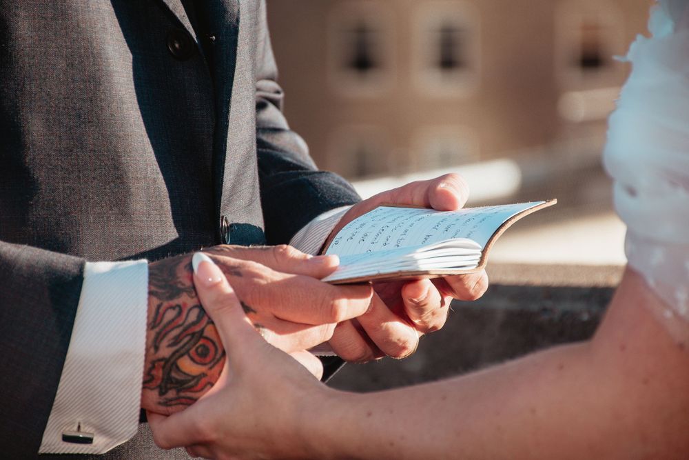 Close up of hands holding a book during wedding ceremony outdoors.