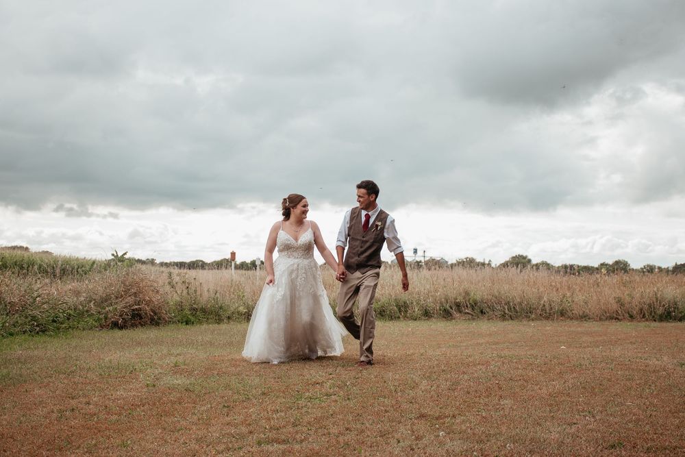 A romantic wedding couple walks through a field under moody gray skies.