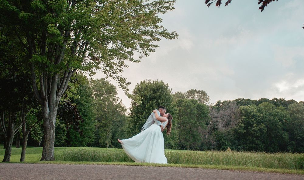 A romantic wedding couple dances in a scenic park setting at dusk.