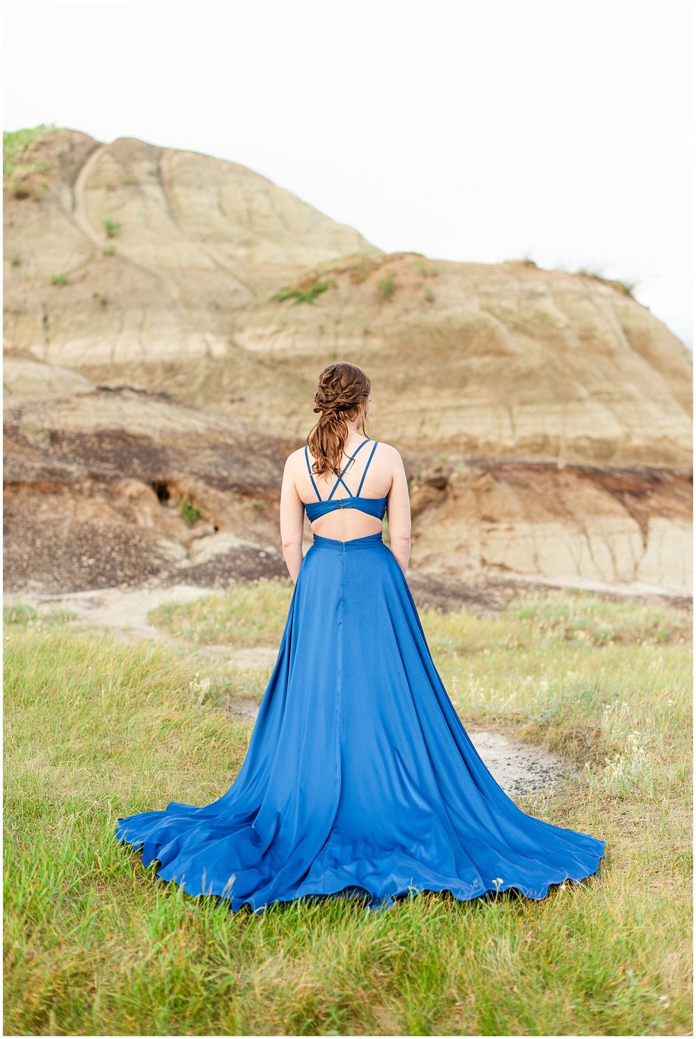 Blue formal gown with dramatic train photographed from behind against rocky badlands terrain.