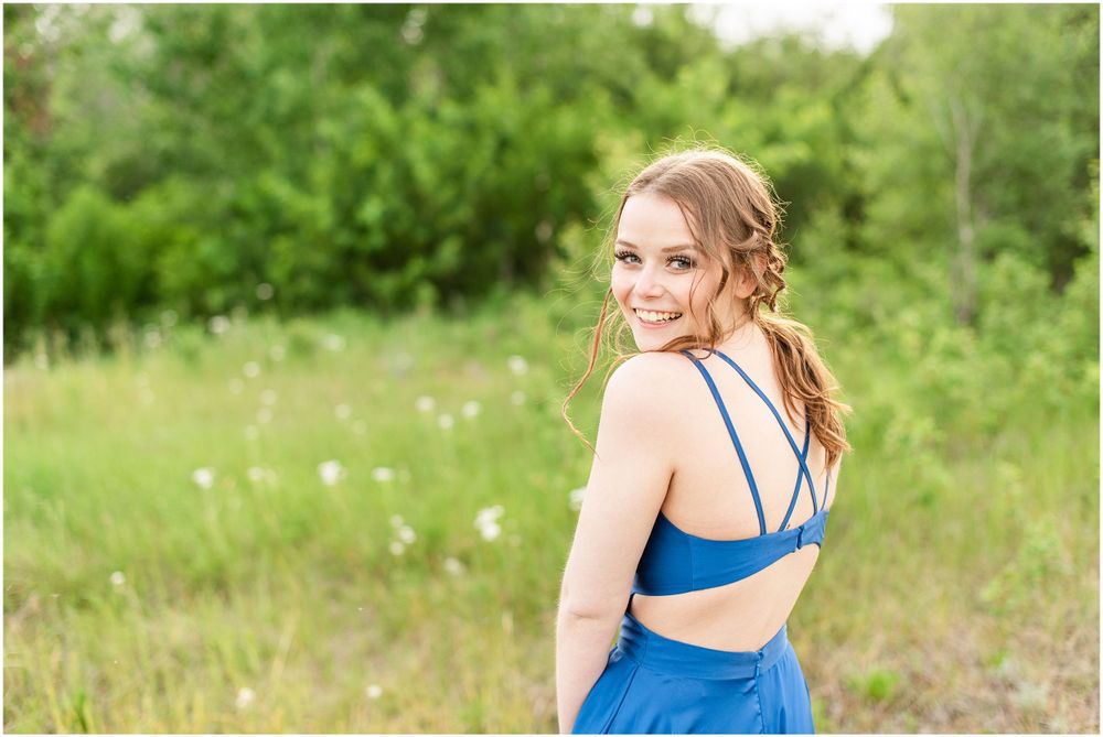 Bright blue formal dress with cutout detail photographed in sunlit meadow setting.