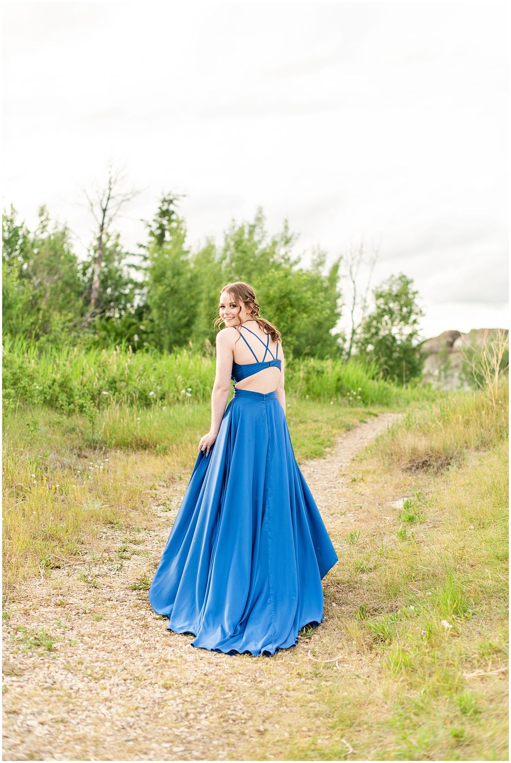 Long blue formal dress with flowing skirt photographed on rustic dirt path.