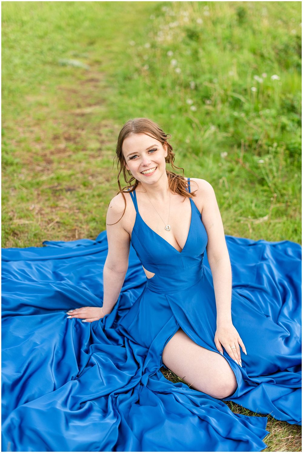 Flowing royal blue formal dress spread out on grass in outdoor portrait setting.