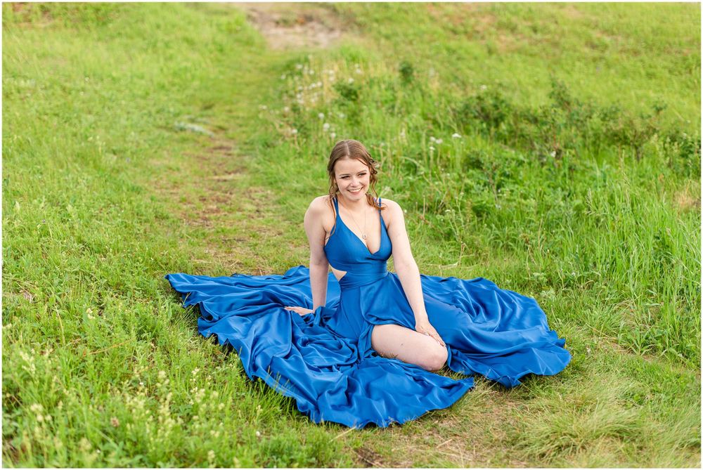 Elegant blue dress with ruffled fabric spread across green grass in outdoor setting.