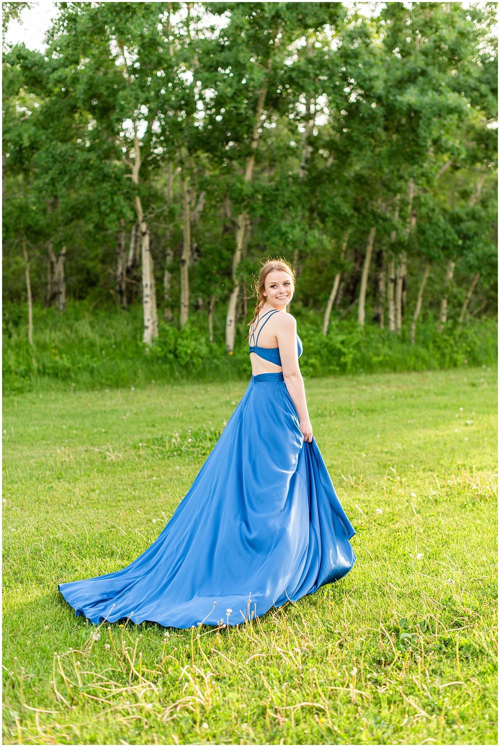 Long royal blue gown with dramatic train photographed in front of wooded background.