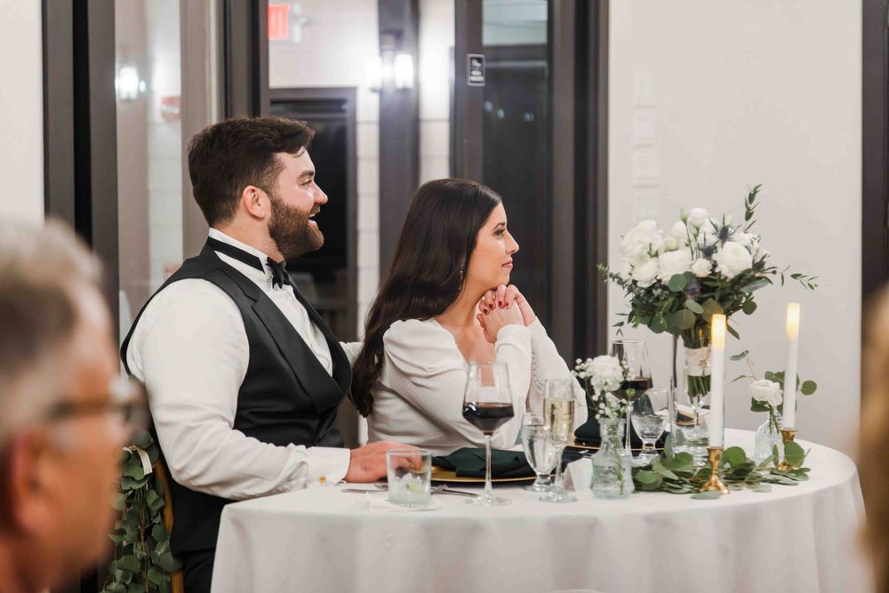 Wedding guests seated at an elegant table with white linens and floral centerpieces during an evening reception.