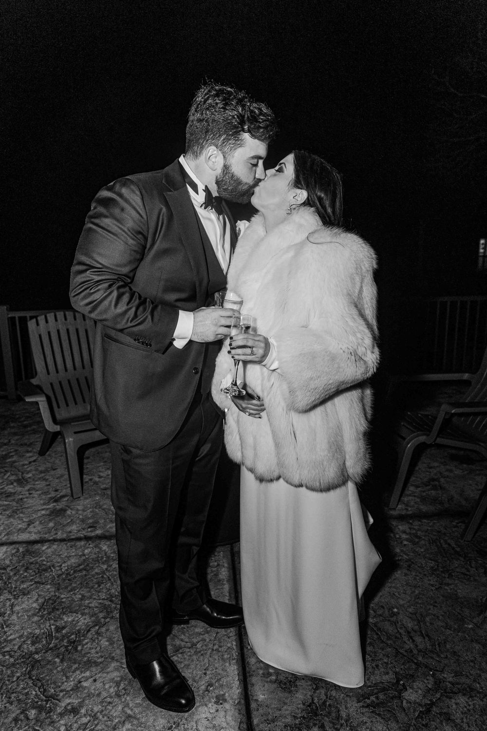 A couple shares an intimate moment at a nighttime wedding reception, with the bride wearing a fur wrap over her gown.