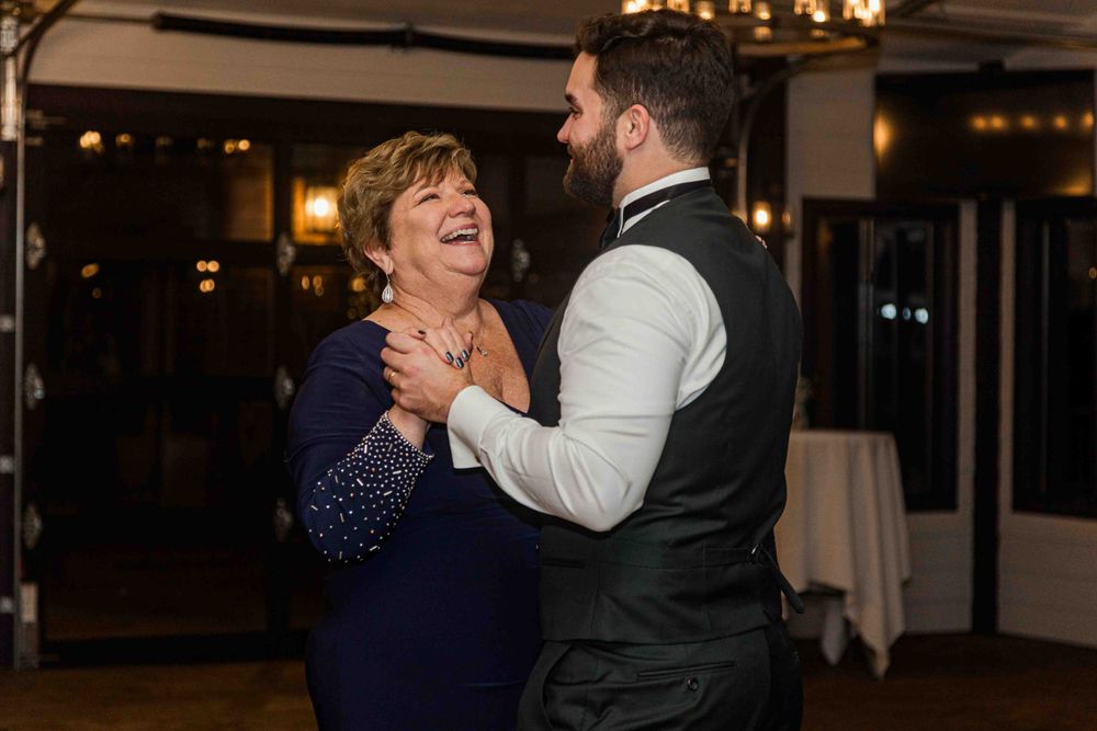A pair of dancers share a joyful moment on the dance floor, with one wearing a navy blue dress and the other in a vest.