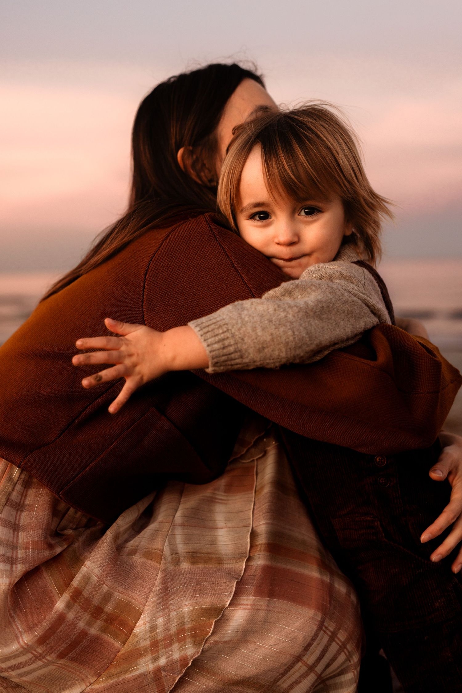 A tender embrace captured at sunset in Denia , as a small child hugs someone wearing a brown coat in soft golden light. Denia photographer