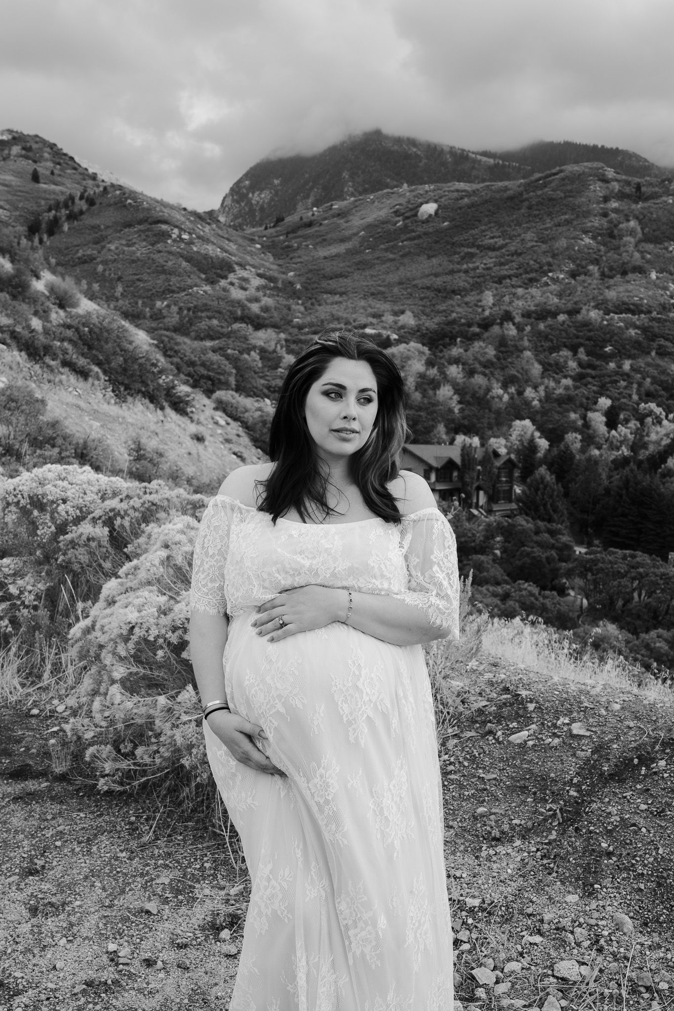 Black and white maternity photo of pregnant woman in lace dress with mountain backdrop.