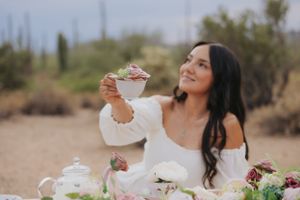 Elegant tea party setup in desert landscape with pink roses and white teacups against saguaro cactus backdrop.