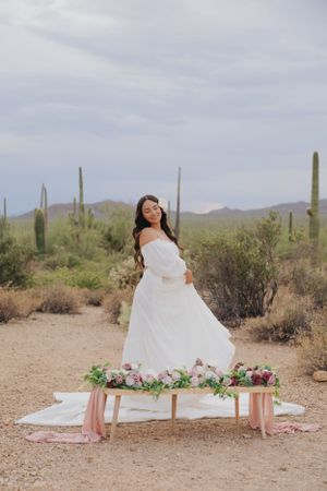 White dress against desert landscape with saguaro cacti and pink floral arrangements.