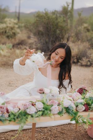 White dress flowing in desert breeze with pink and purple floral arrangements.
