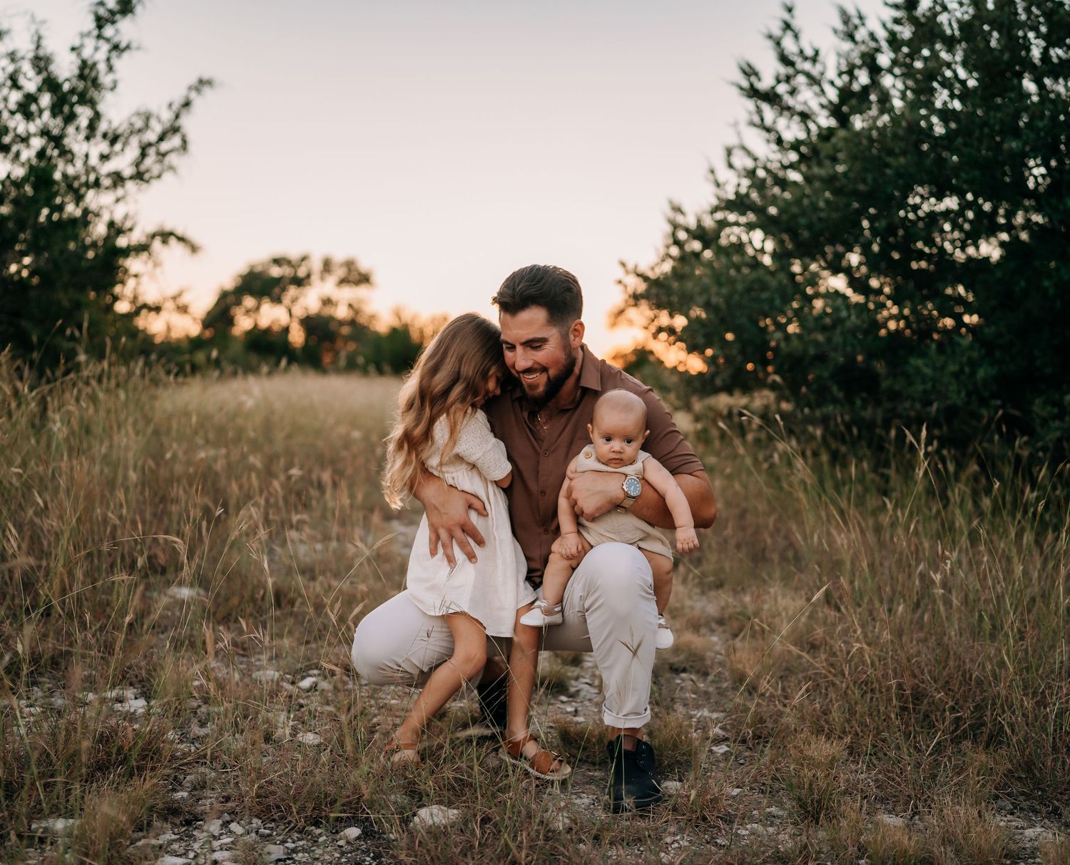 A tender family moment at sunset in a grassy field during a lifestyle photoshoot.