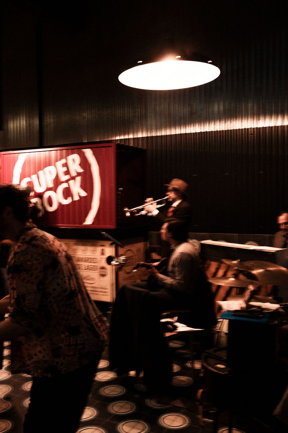 Dimly lit nightclub scene with Super Bock sign and performers on stage.