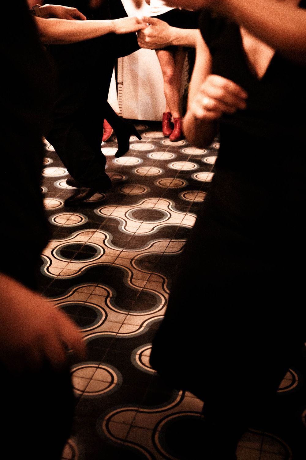 Illuminated geometric floor pattern visible between dancing feet at a nightclub.