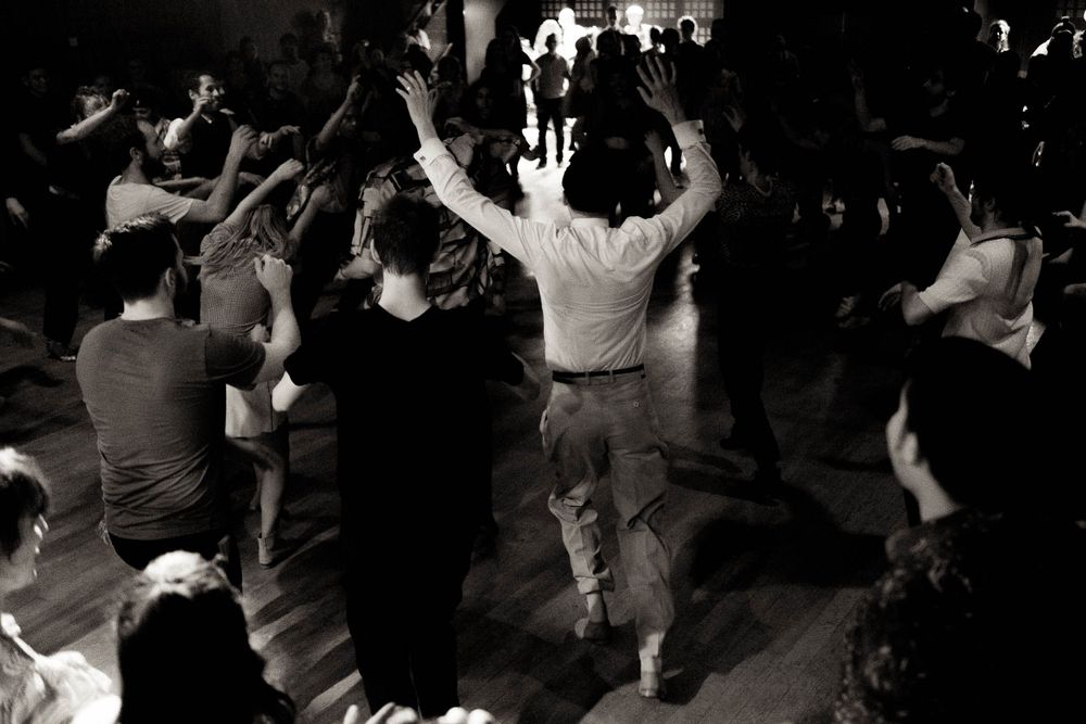 Black and white shot of people dancing with raised arms in a crowded club atmosphere.