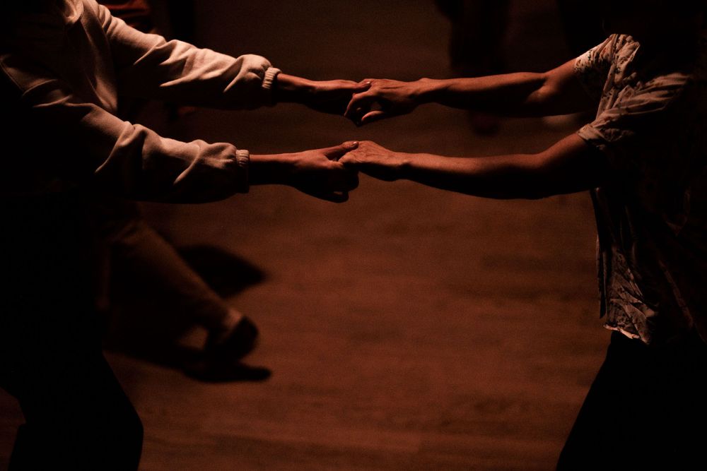 Dancers reaching out with extended arms in a dramatic low-light setting.