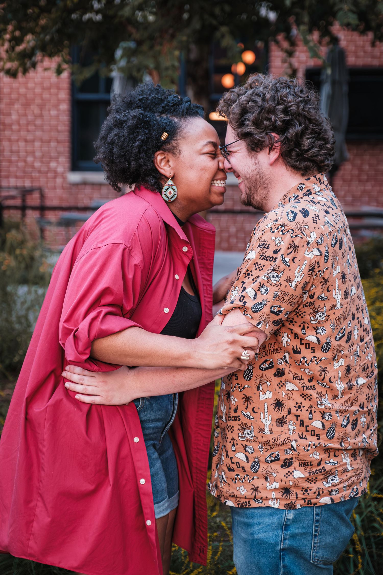 A couple shares a joyful intimate moment together outdoors by a brick building at dusk.