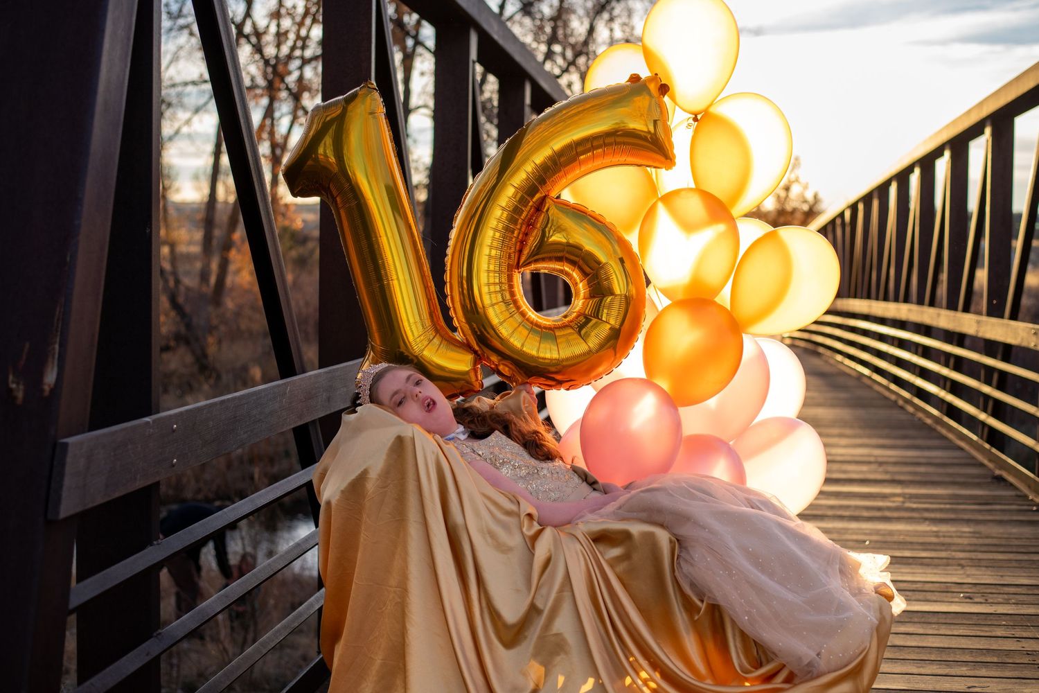 Golden number balloons and peach colored balloons create a festive display on a bridge at sunset.