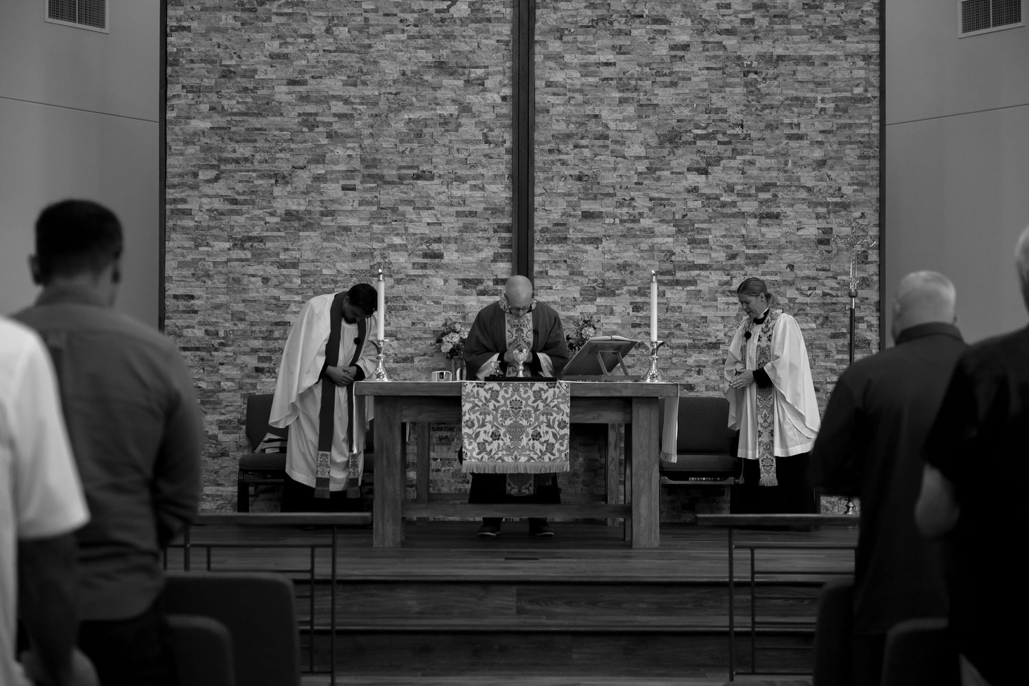 A black and white photograph showing clergy members conducting a religious service at an altar with a stone wall backdrop.