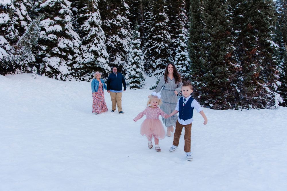 A group plays together in a snowy winter wonderland surrounded by snow-covered evergreen trees.